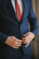 A young groom man businessman in a blue suit and a red tie button his jacket. Finger-ring