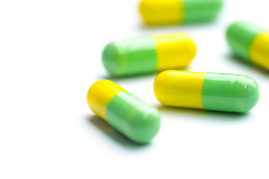 Green and yellow capsules on white background. Group of medication pills.