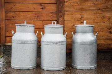 Three milk metal containers in front of a wooden wall