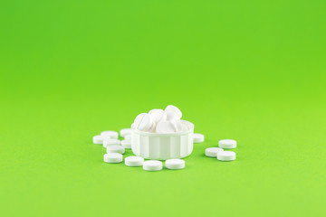 Close up white pills and capsules in cap on green background with copy space. Focus on foreground, soft bokeh. Pharmacy drugstore concept