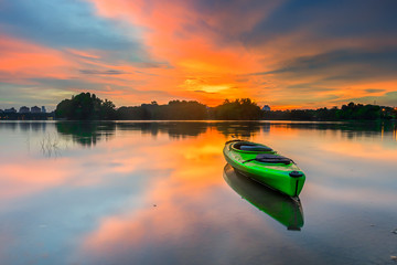 Green canoe on the lake with amazing sunset background.