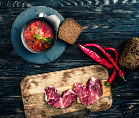 Ceramic bowl of homemade traditional ukrainian borsch with rye bread, paper and meat on the wooden board. Top view. View from above