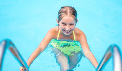 Cute smiling little girl in a swimming pool, looking into the camera