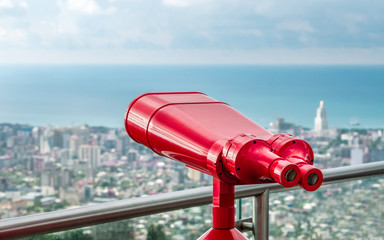Coin operated red binocular towerviewer on observational deck with view on the sea and city