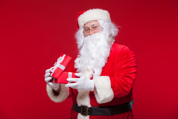 Christmas. Photo Santa Claus giving xmas present and looking at camera, on a red background