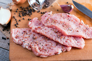 Tenderization of fresh pork steak on wooden chopping board on wooden desk