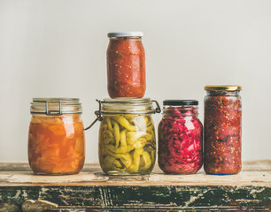 Autumn seasonal pickled or fermented colorful vegetables in glass jars placed in stack over vintage kitchen drawer, white wall background, copy space. Fall home food preserving or canning concept