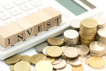 wood word INVEST placed on a calculator with pile of coins as background business concept with copy space.