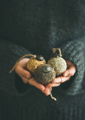 Woman in grey warm woolen sweater holding toy golden and silver decorative balls in hands, copy space, selective focus, vertical composition. Christmas, new year holiday celebration concept