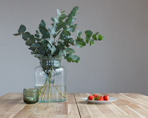 Bouquet of fresh branches of eucalyptus and a plate of ripe strawberries on a large wooden table.