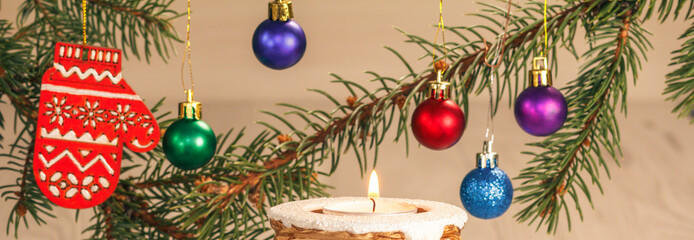 Burning candle and natural fir tree branches with Christmas ornament on grey wooden boards