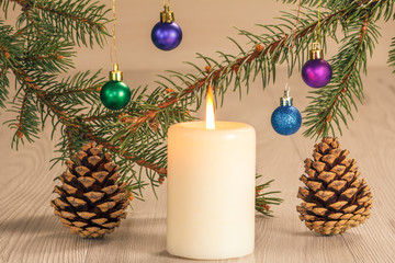 Burning candle and natural fir tree branches with Christmas ornament on grey wooden boards