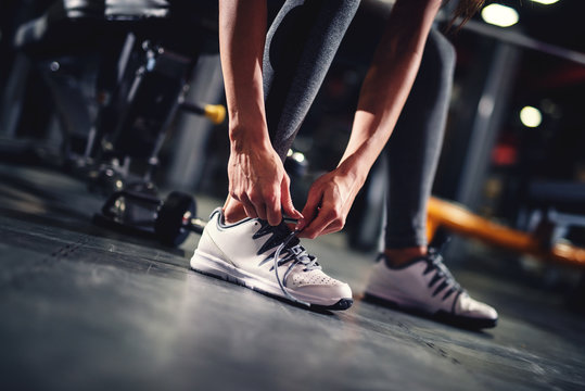 Woman's hand tying shoelaces in the gym near the dumbbells before exercising close up.