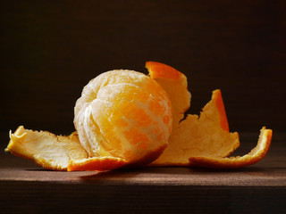 Peeled mandarin on a wooden dark background. Fruit of tangerine without skin. Soft side light on the dark. Healthy eating concept, vegetarian, vegetable healthy food.