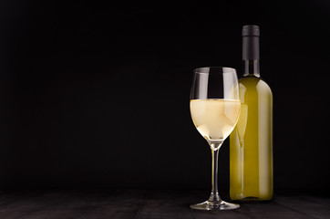 Green bottle of white wine and wine glass mock up on elegant dark black wooden background, copy space.