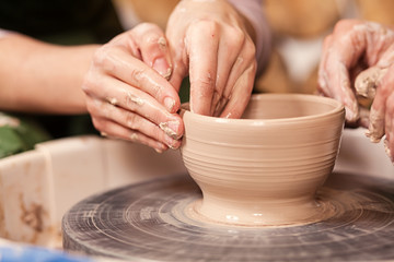 A close-up of the woman's potter teaches the pupil how to make a deep bowl of clay on a potter's wheel in the workshop