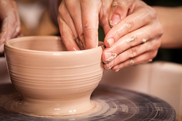 A close-up of the woman's potter teaches the pupil how to make a deep bowl of clay on a potter's wheel in the workshop