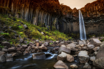 Beautiful waterfall with amazing basalt formations. Waterfalls of Iceland Svartifoss. Water escaping from the waterfall among the stones.
