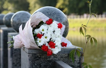 A beautiful bouquet of white chrysanthemums and red roses lies on the green marble handrail of the bridge.