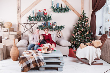 Portrait of young friendly family looking at camera on Christmas morning. Father, mother and daughter