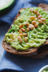 Close-up of the rye bread sandwich with smeared avocado with fried pine nuts on the textured blue background. The concept of health and fitness eating.