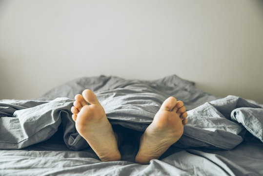 Men's feet under a gray blanket
