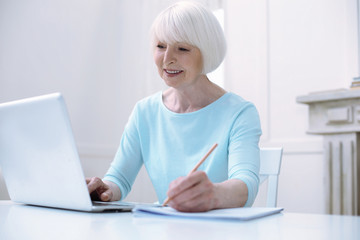 Progressive pensioner. Active progressive cheerful old woman looking happy while working at her laptop