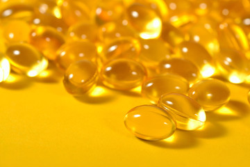 Omega-3 fish fat oil capsules close up on a yellow background.