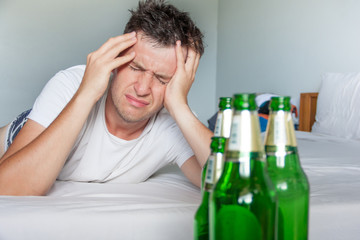 Hangover suffering man holding his aching head close up portrait with bottles of beer. Alcoholism...