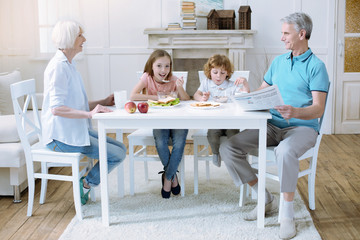 Tasty meal. Cheerful happy friendly relatives sitting at the big white table and eating together