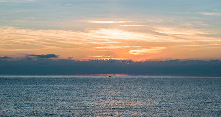 Fototapeta na wymiar Small silhouette of a boat in nice cloudy sunrise scene