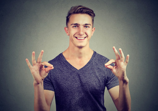 Satisfied happy man gesturing Ok sign isolated on gray background