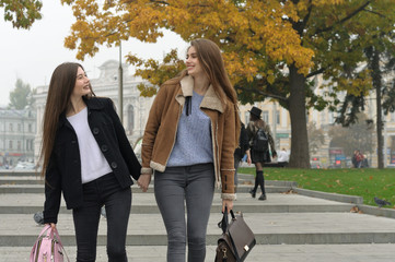 Two girlfriends walk along the steps of the sidewalk holding hands