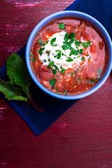 Ukrainian traditional borsch. Russian vegetarian red soup  in blue bowl on red wooden background.  Borscht, borshch with beet.  Top view.