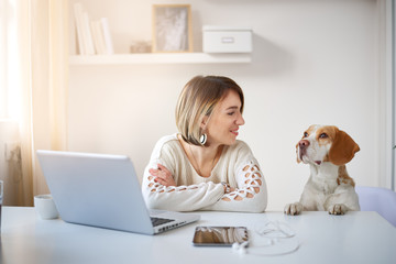 Woman sitting in home office and using laptop while her dog watching