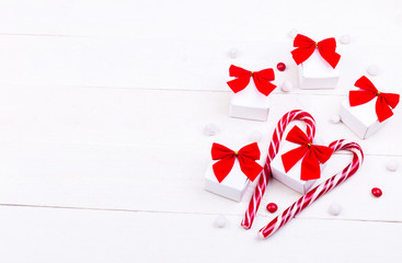 Christmas gifts, white little boxes with red bow  and candies on white wooden background. Flat lay. Merry Christmas.