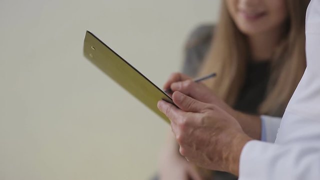 Hands of a doctor writes a medical record to the pregnant woman. Close-up