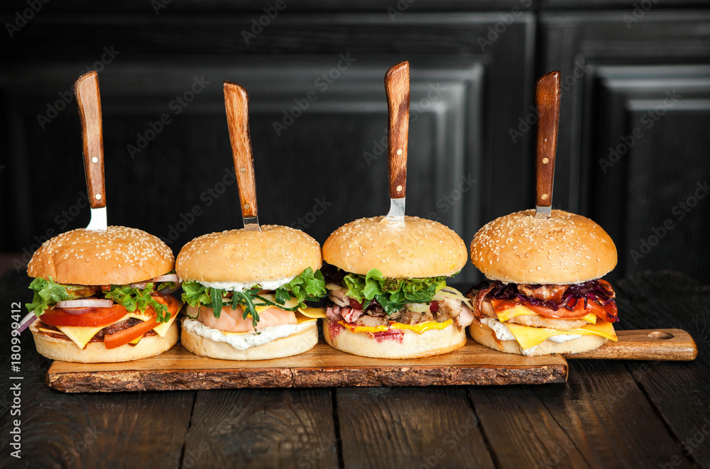 Wall mural four burgers on knives on a wooden surface