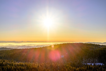 Mountain views. View of the misty Alps. Orange sunset. Snowy trees and valley.