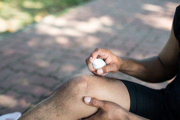Asia young man runner with a knee injury gets cooling spray to relief the pain. concept of injuries...