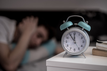 Wecker auf Nachttisch, schlafender junger Mann, gereizt