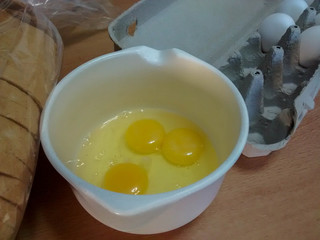 egg yolks and whites in bowl with egg carton and sliced bread, on kitchen counter