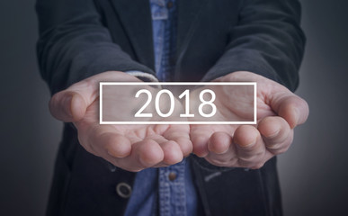 Businessman showing 2018 in hand on dark background