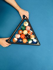 Puramid of pool billiard balls in hands on blue table