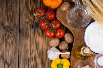 Frische Zutaten für einen traditionellen Pizzateig und Belag mit Tomaten, Pilzen und Knoblauch auf einem Brett aus Olivenholz mit Getreideähren im Hintergrund