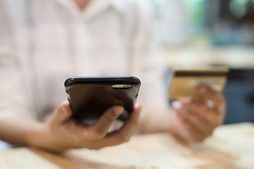 The blurry design background of woman hand is holding credit card and focus at mobile phone in hand for Shopping Online.