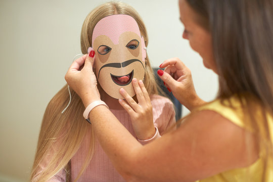 Mother attaching paper mask to daughter's face
