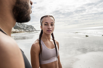Young male and female runners gazing at each other on beach