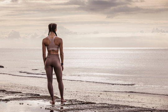 Rear view of young female runner at water's edge looking out to sea