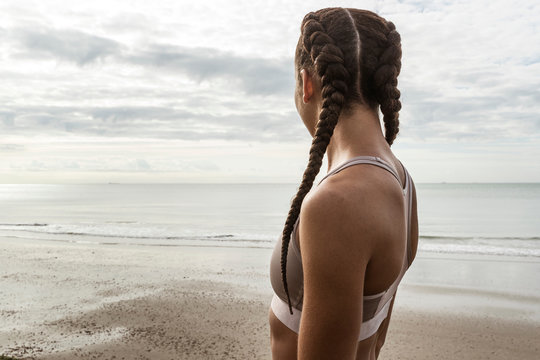 Young female runner with hair plaits looking out to sea from beach
